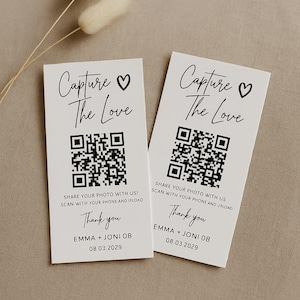 May include: Two white cards with the text "Capture the Love" and a heart symbol. Each card has a QR code, the words "Share your photo with us! Scan with your phone and ipload", "Thank you", and the names "EMMA + JONI 08" with the date "08.03.2029".