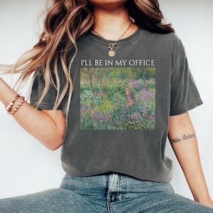 May include: A dark grey t-shirt featuring a painting of a garden scene and the text "I'll be in my office" printed on the front.