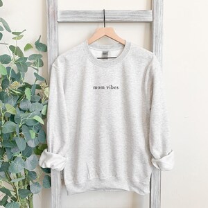 May include: A gray sweatshirt with the text "mom vibes" printed on the front.