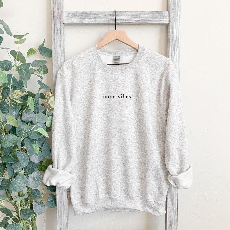 May include: A gray sweatshirt with the text "mom vibes" printed on the front.