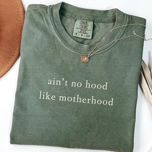 May include: A green t-shirt with the text "ain't no hood like motherhood" printed in white.