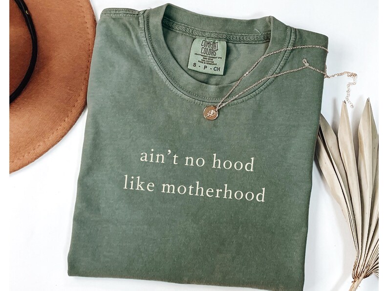May include: A green t-shirt with the text "ain't no hood like motherhood" printed in white.