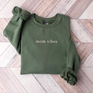 May include: A dark green sweatshirt with the text "mom vibes" printed in white on the front.