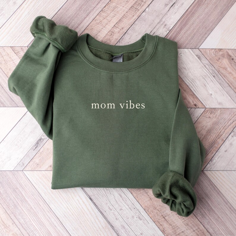 May include: A dark green sweatshirt with the text "mom vibes" printed in white on the front.