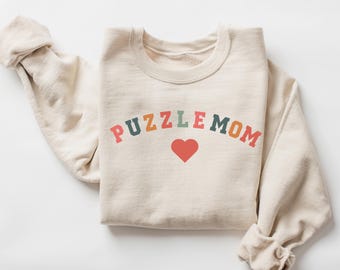 May include: A beige sweatshirt with the text "PUZZLE MOM" in rainbow colors and a red heart in the center.