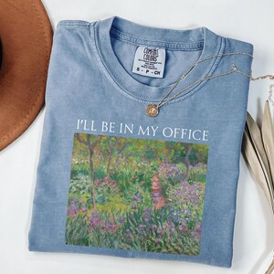 May include: A light blue t-shirt with a vintage-style print of a garden scene and the text "I'll be in my office".