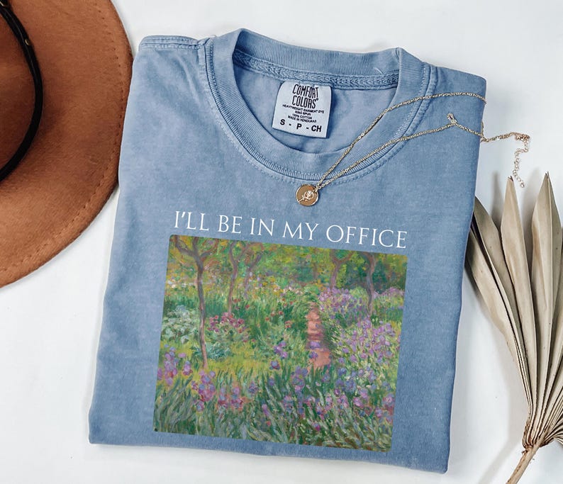 May include: A light blue t-shirt with a vintage-style print of a garden scene and the text "I'll be in my office".