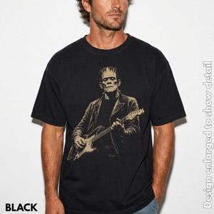 Puede incluir: Una camiseta negra de manga corta con un estampado gr&aacute;fico en color beige de una figura que se asemeja al monstruo de Frankenstein tocando una guitarra el&eacute;ctrica. El dise&ntilde;o est&aacute; centrado en el pecho y muestra al personaje con una chaqueta.