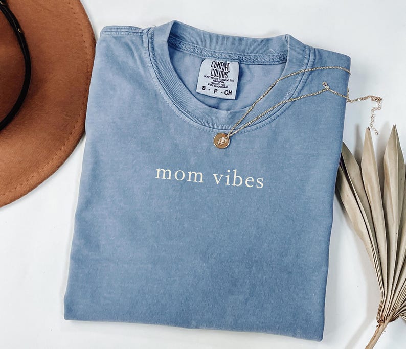 May include: A light blue t-shirt with the text "mom vibes" in white lettering. The shirt is made of a soft, comfortable material.