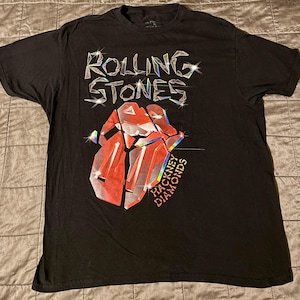 May include: Black t-shirt featuring the Rolling Stones logo with a red and silver graphic of the band's iconic tongue and lips design. The text "HACKNEY DIAMONDS" is below the graphic.