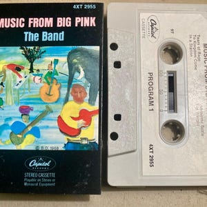 May include: A vintage cassette tape with a black and white illustration of a band on the front. The tape is titled "Music From Big Pink - The Band" and features the Capitol Records logo. The tape is labeled "4XT 2955" and is a stereo cassette.