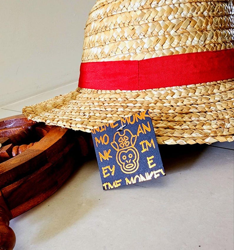 May include: A straw hat with a red band and a black tag that says "Anime Monkey" with a monkey graphic in gold. The tag also says "Monkey D. Luffy" in gold.