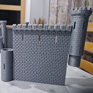 May include: A gray, 3D-printed castle model with a brick pattern. The model features a wall with crenellations, a cylindrical tower, and a turret. The castle is designed for tabletop gaming or display.