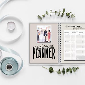 以下が含まれることがあります： ベージュの表紙に大きな黒い文字で「Wedding Planner」と書かれた、スパイラル綴じのウェディングプランナー。プランナーは、結婚式の予算チェックリストのあるページに開かれています。左側には、花嫁、新郎、ウェディングドレスの写真があります。