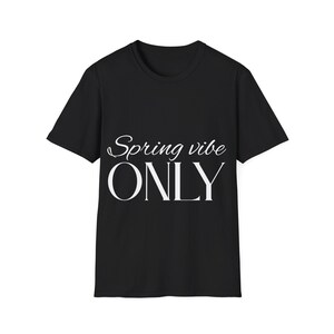以下が含まれることがあります： 白文字で「Spring vibe ONLY」と書かれた黒いTシャツ。テキストは筆記体とブロック体の組み合わせです。Tシャツはクルーネックで、柔らかい素材で作られているようです。テキストは前面の中央に配置されています。