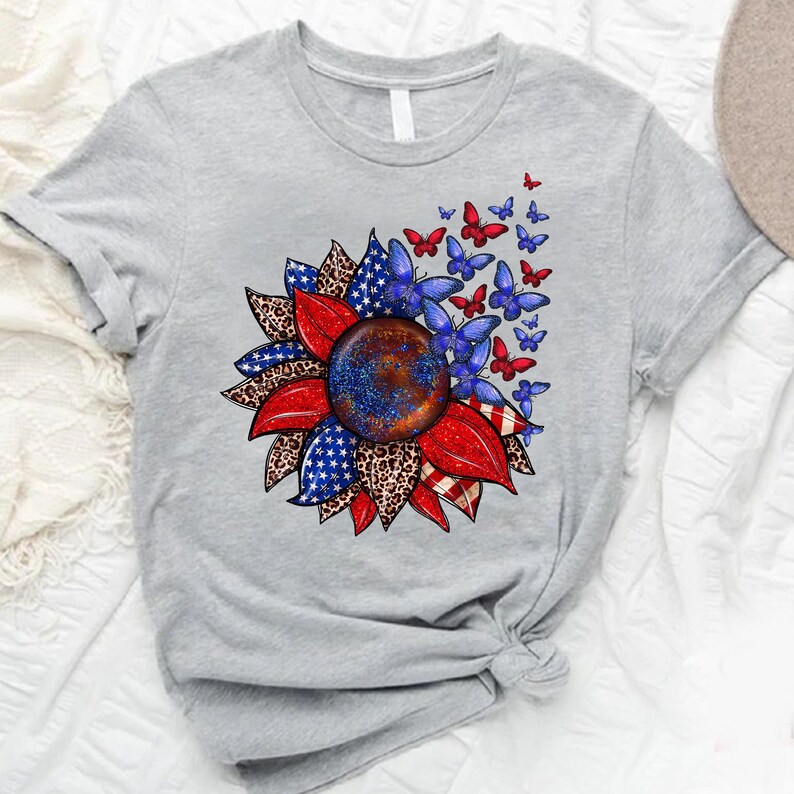 A gray t-shirt with a vibrant graphic design featuring a sunflower surrounded by butterflies in red, blue, and white colors.