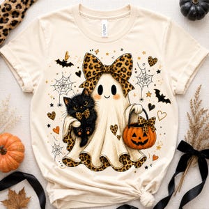 A white t-shirt with a Halloween-themed design featuring a ghost, a cat, a pumpkin, and various Halloween symbols.