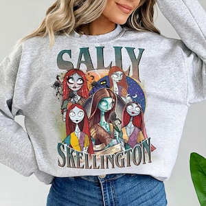 Może przedstawiać: Jasnoszara bluza z nadrukiem Sally z filmu Miasteczko Halloween. Grafika zawiera napis "SALLY" nad okrągłym obrazem postaci Sally i napis "SKELLINGTON" poniżej.