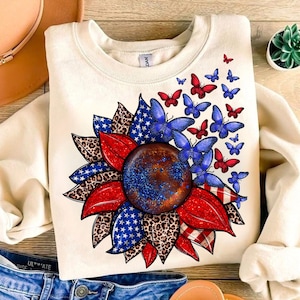 A white sweatshirt with a patriotic design featuring a sunflower surrounded by butterflies and stars.