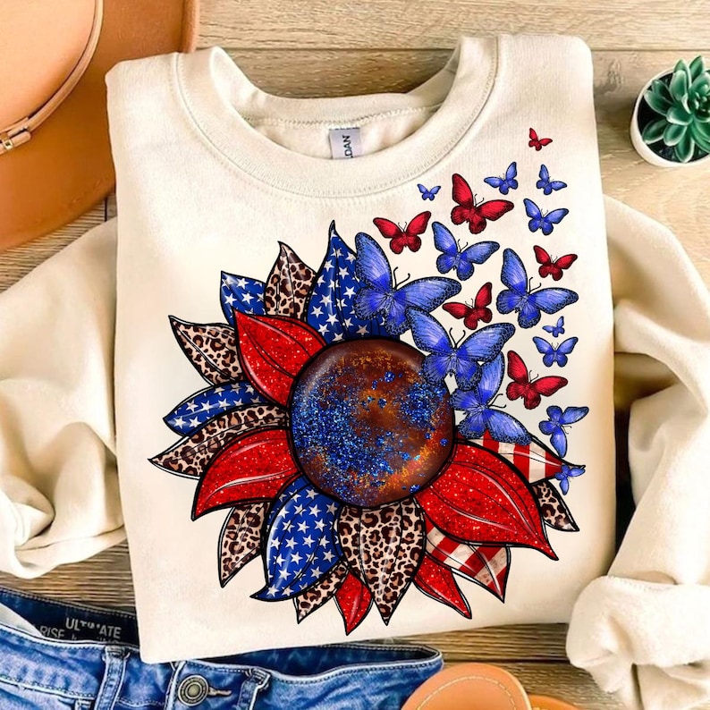 A white sweatshirt with a patriotic design featuring a sunflower surrounded by butterflies and stars.
