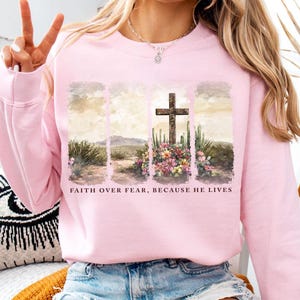 May include: Pink sweatshirt with a graphic of a wooden cross in a desert landscape with the text "Faith over fear, because he lives".