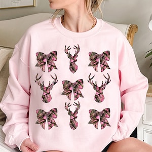 a woman sitting on a bed wearing a pink sweatshirt with bows on it
