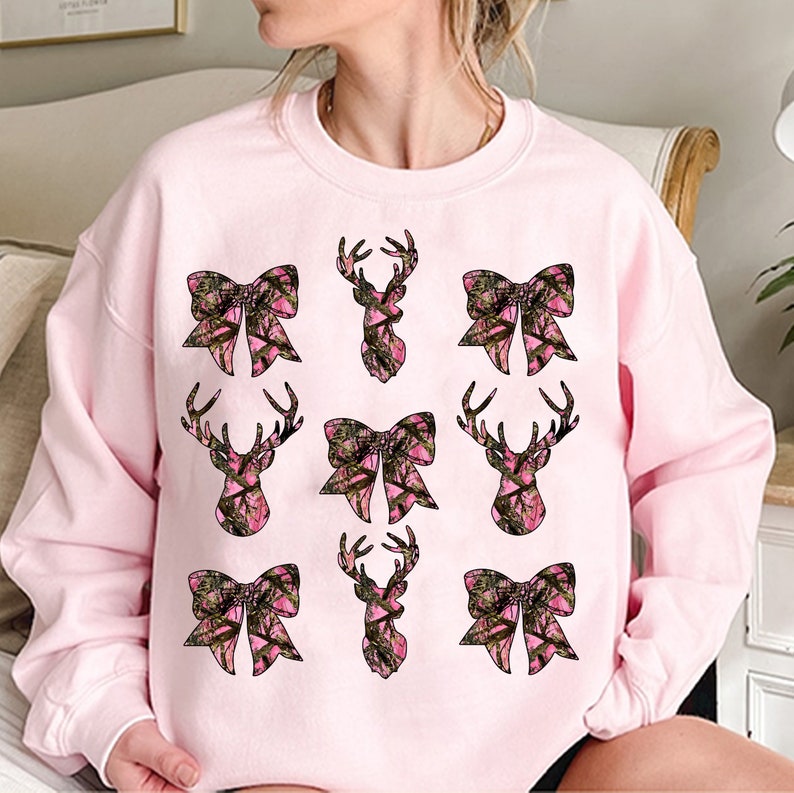 a woman sitting on a bed wearing a pink sweatshirt with bows on it