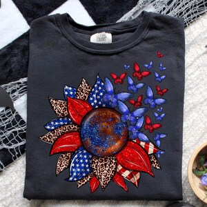 a black t-shirt with a vibrant design of a sunflower surrounded by butterflies and leopard print leaves.