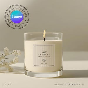 Puede incluir: Una vela blanca en un tarro de vidrio transparente con una etiqueta que dice "white JASMINE AROMATIC CANDLE". La vela está encendida y la llama es visible. La vela está sobre una superficie blanca.
