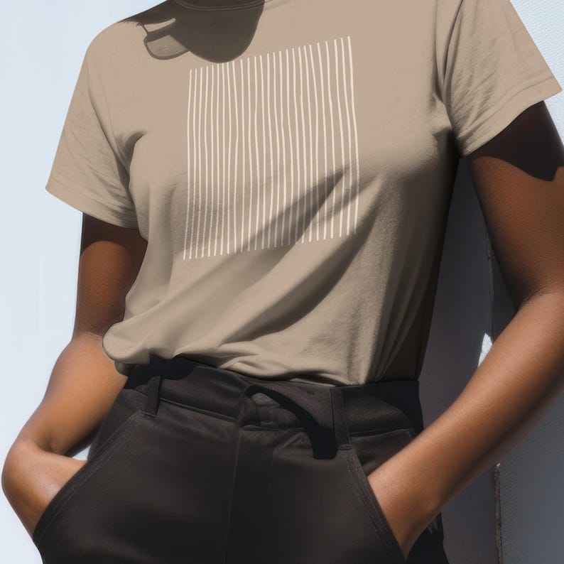 May include: A tan t-shirt with a white vertical stripe design. The shirt is short-sleeved and has a crew neck. The person is wearing black pants.