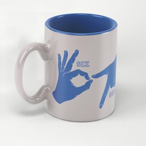 May include: White ceramic mug with a blue interior and handle. The mug features blue hand gestures spelling out the numbers "SIX" and "SEVEN". A unique and playful design for coffee or tea.