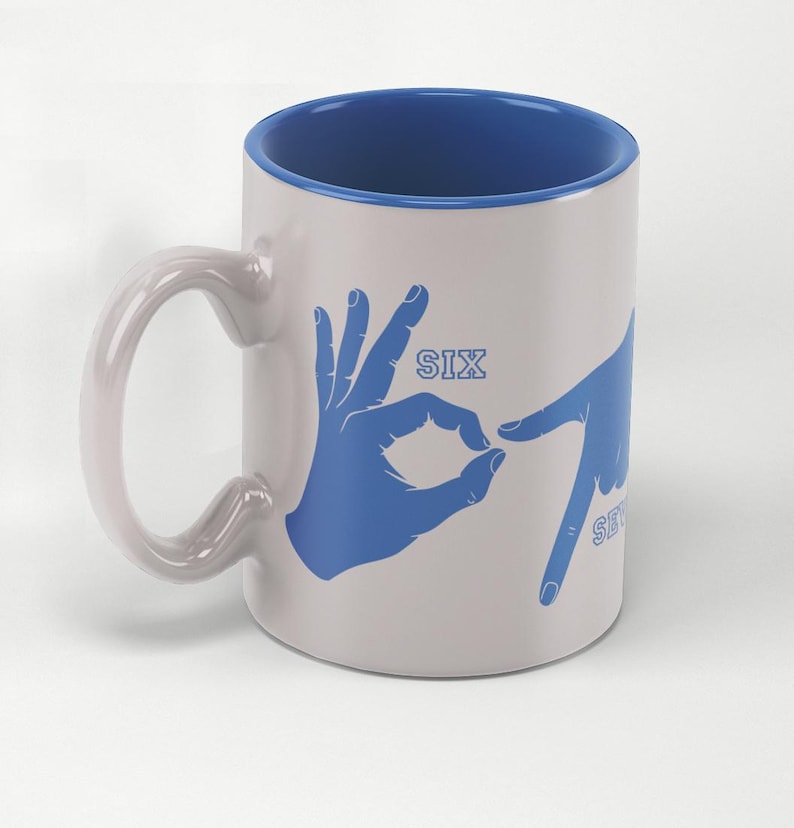 May include: White ceramic mug with a blue interior and handle. The mug features blue hand gestures spelling out the numbers "SIX" and "SEVEN". A unique and playful design for coffee or tea.