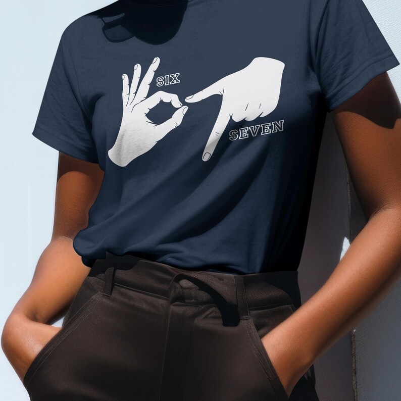 May include: Navy blue t-shirt with a white graphic of two hands forming the numbers six and seven in American Sign Language. The word "SIX" is above the hand forming the number six, and the word "SEVEN" is next to the hand forming the number seven.