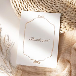 May include: A white card with a gold frame and the text "Thank you!"  The card is sitting on a woven straw mat and a beige fabric.