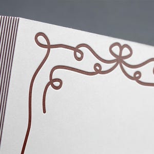 May include: A white card with a decorative border of brown, curly lines. The border is reminiscent of a ribbon or a vine.