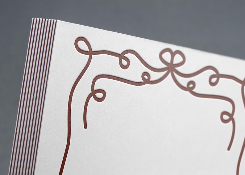 May include: A white card with a decorative border of brown, curly lines. The border is reminiscent of a ribbon or a vine.