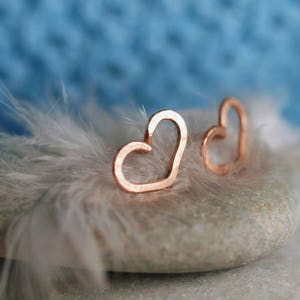 Puede incluir: Dos delicados pendientes en forma de coraz&oacute;n de oro rosa sobre una pluma blanca y una piedra gris.