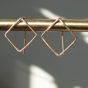 May include: A pair of gold-toned diamond-shaped earrings with a simple, minimalist design.