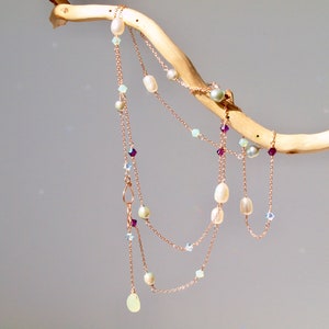 May include: A delicate layered necklace featuring white pearls, light blue and purple crystals, and a light green stone pendant.