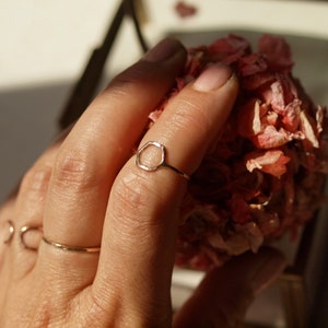 Può includere: Un anello d'oro con forma esagonale. L'anello è su un dito e lo sfondo è sfocato.