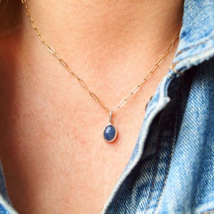Op de afbeelding: Een delicate gouden ketting met een klein, ovaalvormig hanger met een donkerblauwe edelsteen.