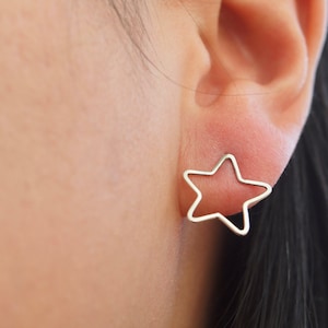 May include: A close-up of a person's ear with a silver star-shaped earring. The earring is a simple, open design.