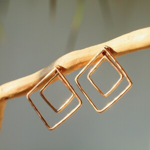 Peut inclure: Une paire de boucles d'oreilles géométriques dorées avec un design carré double. Les boucles d'oreilles sont en fil métallique et ont une texture martelée.