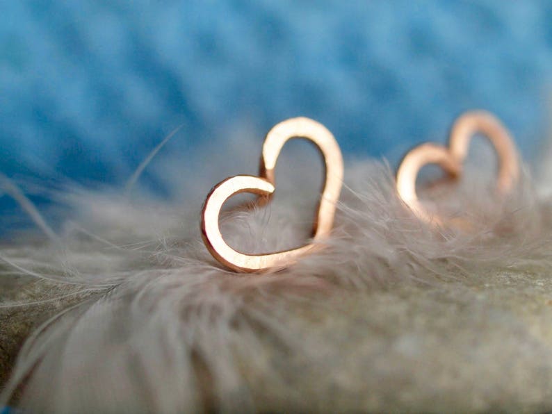 Puede incluir: Dos pendientes de coraz&oacute;n de oro sobre un fondo de plumas blancas.