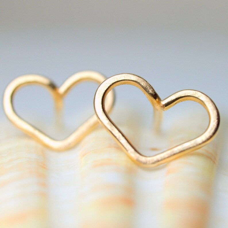 Puede incluir: Un par de pendientes de coraz&oacute;n de oro. Los pendientes son simples y delicados, con un acabado liso y pulido.