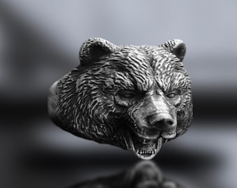 May include: A silver bear head ring with a detailed, textured design. The bear's mouth is open, showing its teeth.