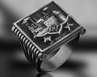 Puede incluir: Un anillo de plata con un diseño 3D detallado de una ciudad, que incluye una torre y otros edificios. El anillo tiene una cara cuadrada y una banda gruesa.
