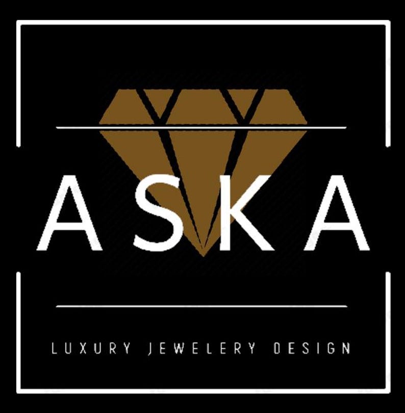 Op de afbeelding: Logo voor luxe sieradenontwerp, met het woord "ASKA" in witte hoofdletters boven de woorden "LUXURY JEWELRY DESIGN" in kleinere witte letters. Het logo bevat een bruine diamantvorm en is geplaatst tegen een zwarte achtergrond, omlijst door een witte rand.