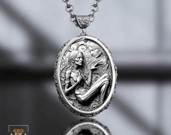May include: An oval silver pendant necklace featuring a detailed relief sculpture of a thin, seated figure with long hair and a second ethereal face above, suspended from a thick silver chain. The metal has a dark, oxidized finish.