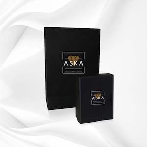 Op de afbeelding: Twee zwarte sieradendoosjes van verschillende formaten. Beide dozen hebben het woord "ASKA" in het wit, met een gouden diamantafbeelding en de tekst "LUXURY JEWELLERY DESIGN" in het wit. De dozen staan op een witte achtergrond.